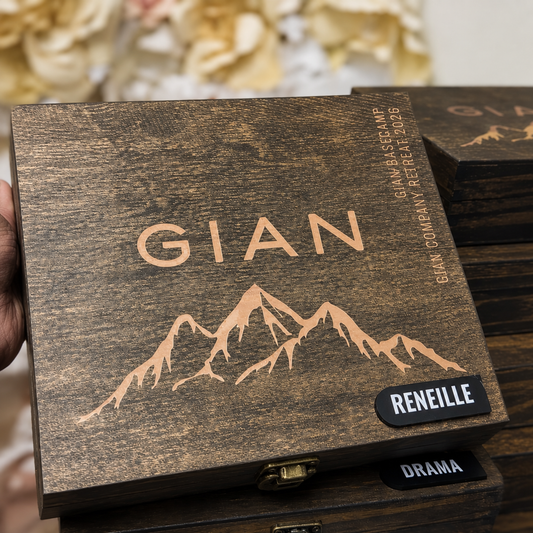 A close-up of a dark wood keepsake box with laser-engraved copper text and mountain graphics. The front lid shows the name 'GIAN' in large copper letters above a mountain outline, with additional engraving along the right side.